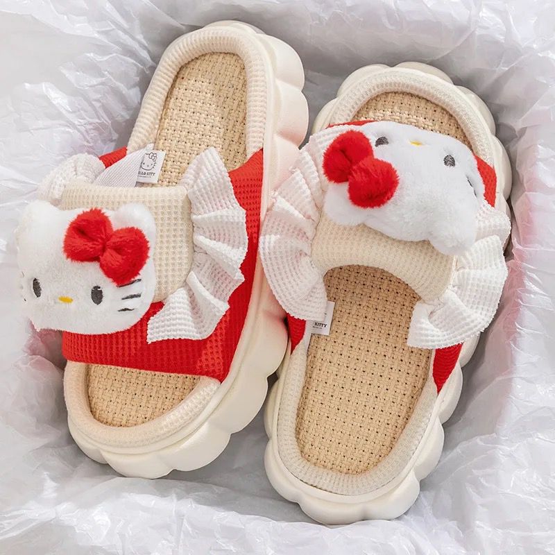 A pair of white slippers with red accents and Hello Kitty characters on the top, placed on a soft, grey surface.
