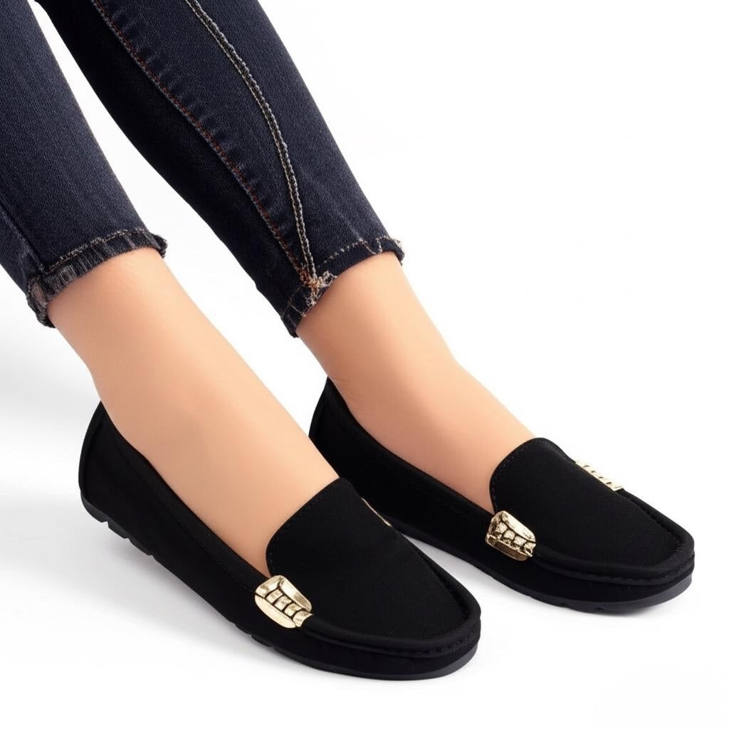 Black loafers with gold accents worn with dark jeans on a white background