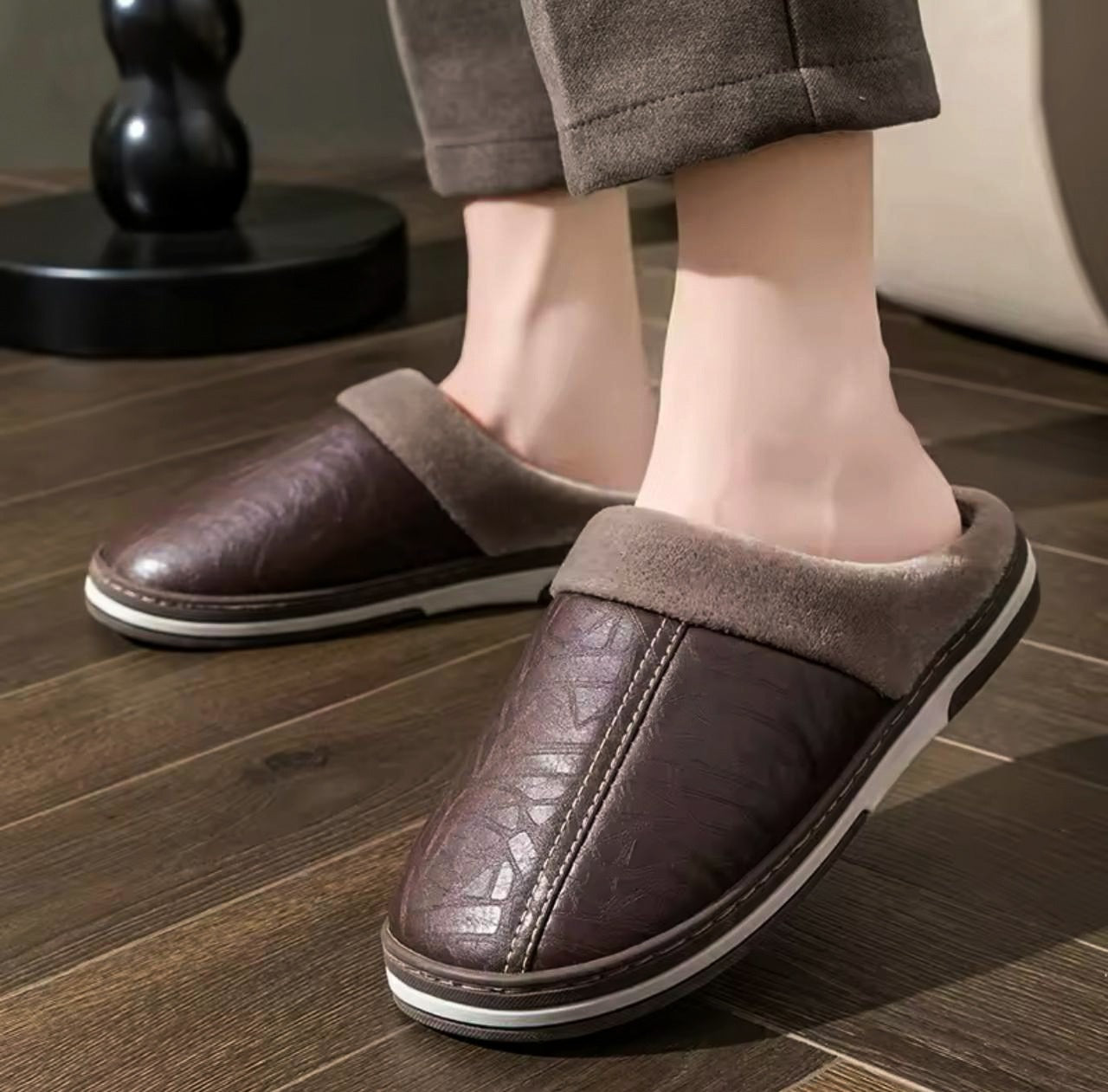 A person wearing brown faux leather half shoes with plush fur lining on a wooden floor.