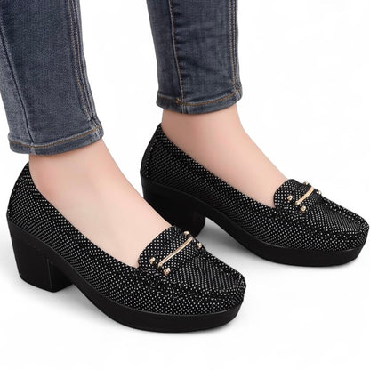 Black shoes with gold accents worn with blue jeans on a white background