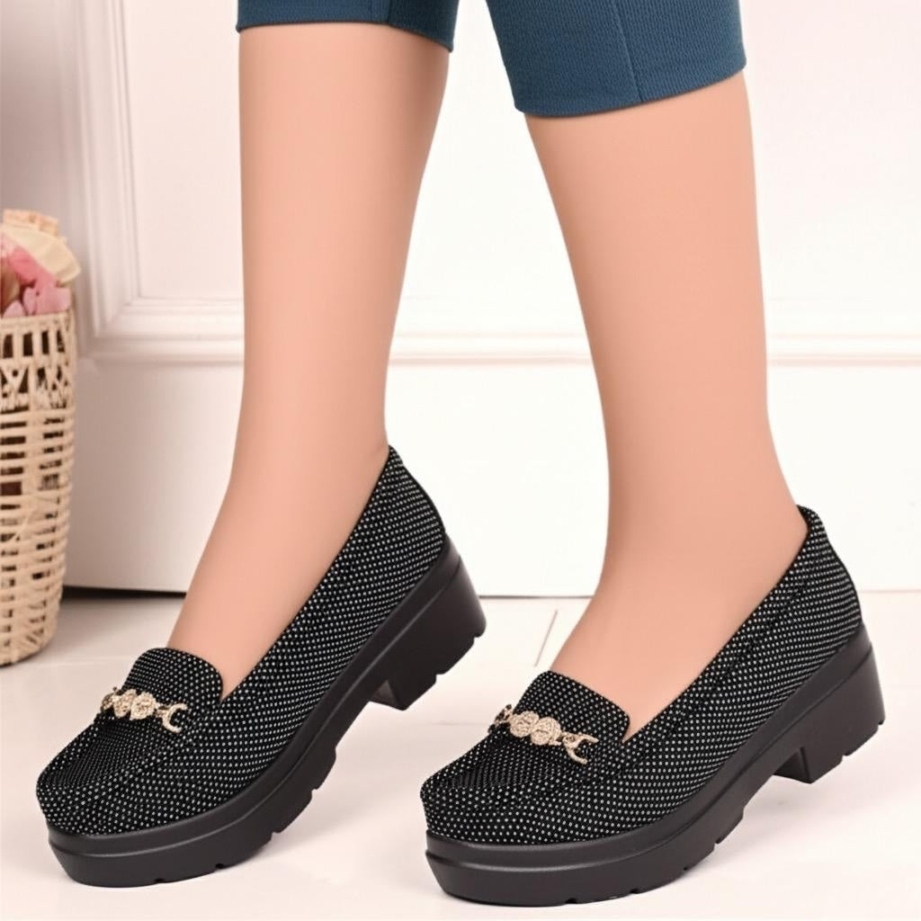 Black platform shoes with decorative elements worn by a person on a light background