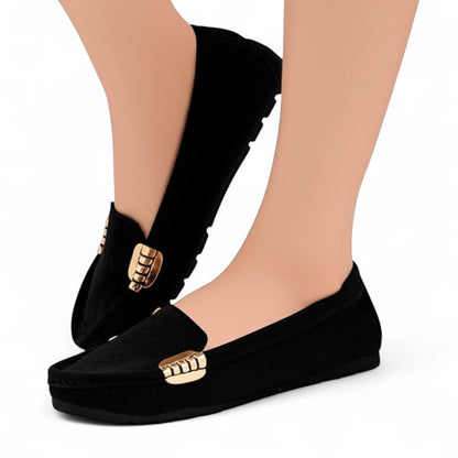 Black loafers with gold accents worn by a person on a white background