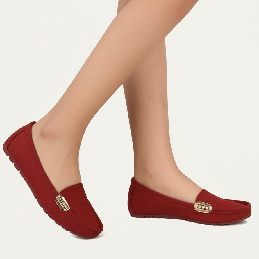 Red loafers with gold accents worn by a person on a white background