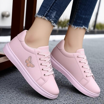 Pink sneakers with a butterfly design worn by a person on a textured surface.