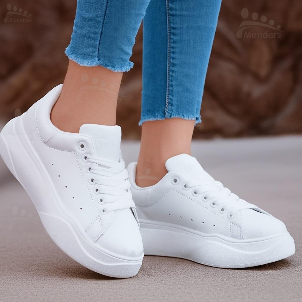 White sneakers worn with blue jeans on a neutral background